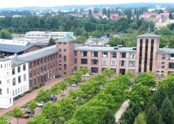 Luftbild von Guben mit einem langgestreckten Backsteinbau, Bäumen und Dächern der Stadt