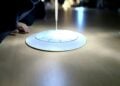 Eine selbst gebastelte Sonnenuhr aus Pappe liegt im Lichtkegel auf einem Tisch, daneben die Hand eines Kindes