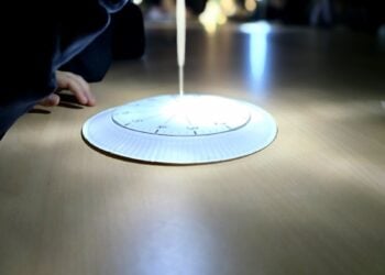 Eine selbst gebastelte Sonnenuhr aus Pappe liegt im Lichtkegel auf einem Tisch, daneben die Hand eines Kindes