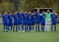 Die Spieler des SV Blau-Weiß 19 Lichterfeld in blauen Trikots stehen Arm in Arm auf dem Rasen