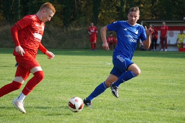 Ein Lichterfelder Spieler in Blau und ein Kostebrauer Spieler in Rot laufen zum Ball