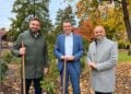 Drei Männer mit Spaten stehen im Herbstlaub hinter einem frisch gepflanzten Rosenstrauch