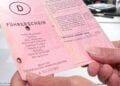 Zwei Hände halten einen alten rosafarbenen Papierführerschein