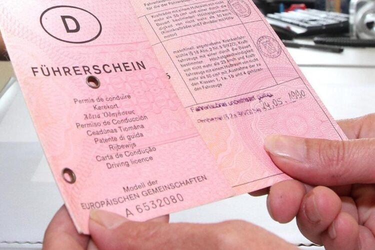 Zwei Hände halten einen alten rosafarbenen Papierführerschein