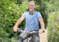 Mann mit Brille auf einem Fahrrad auf einem Weg zwischen grünen Hecken