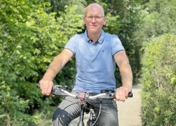 Mann mit Brille auf einem Fahrrad auf einem Weg zwischen grünen Hecken