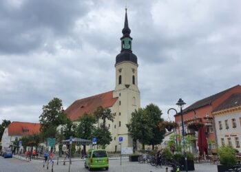 Kirchplatz in Lübbenau mit der Nikolaikirche und Häusern der Altstadt unter bewölktem Himmel