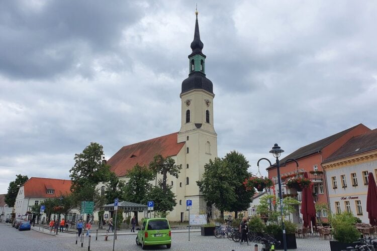 Kirchplatz in Lübbenau mit der Nikolaikirche und Häusern der Altstadt unter bewölktem Himmel