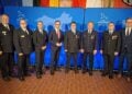 Acht Männer in Feuerwehruniform und Anzug stehen nebeneinander vor einer blauen Wand mit dem Logo des Landes Brandenburg