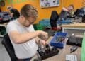 Bürgermeister Andreas Pfeiffer schraubt an einer Werkbank einen geöffneten mechanischen Stromzähler auseinander