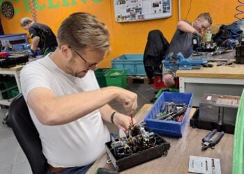 Bürgermeister Andreas Pfeiffer schraubt an einer Werkbank einen geöffneten mechanischen Stromzähler auseinander
