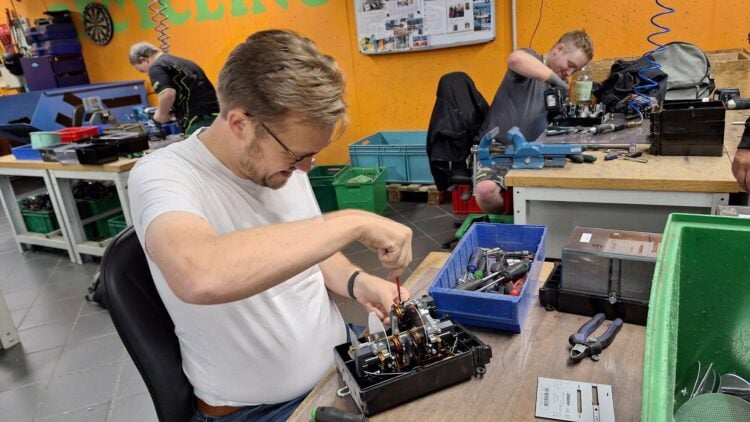 Bürgermeister Andreas Pfeiffer schraubt an einer Werkbank einen geöffneten mechanischen Stromzähler auseinander