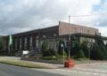 Backsteinbau des BASF-Kulturhauses in Schwarzheide mit Treppe, Grünanlage und Straße im Vordergrund