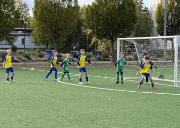 Nachwuchsfußballer in grünen sowie gelb-blauen Trikots auf einem Kunstrasenplatz vor einem Tor