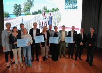 Gruppenfoto auf einer Bühne mit mehreren Personen, die große symbolische Förderbescheide halten