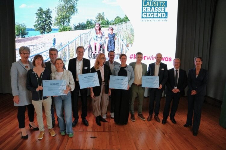Gruppenfoto auf einer Bühne mit mehreren Personen, die große symbolische Förderbescheide halten