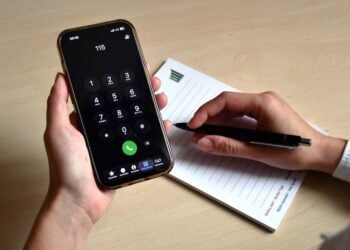 Hand hält ein Smartphone, auf dem die Nummer 115 gewählt ist, daneben ein Notizblock