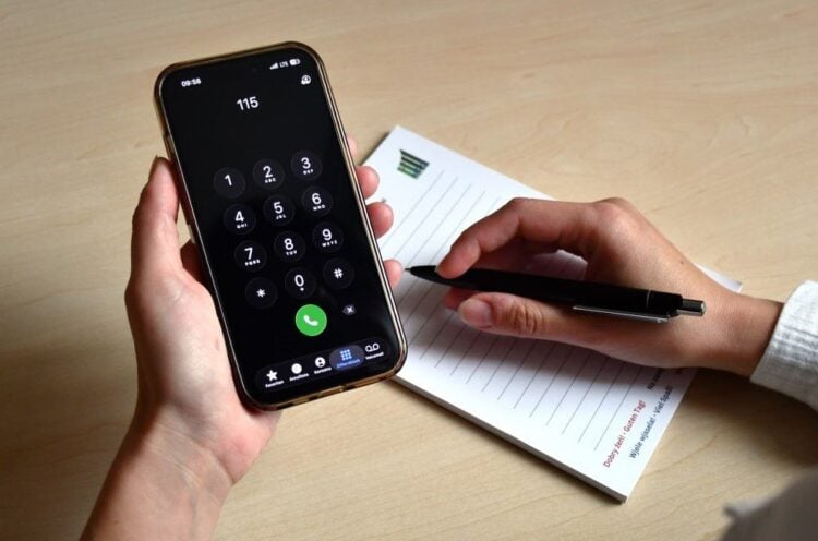 Hand hält ein Smartphone, auf dem die Nummer 115 gewählt ist, daneben ein Notizblock