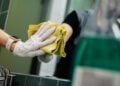 Hand in weißem Einweghandschuh poliert mit gelbem Tuch einen Spiegel über einem Waschbecken