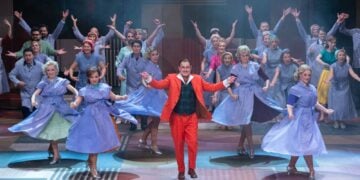 Szenenfoto aus Messeschlager Gisela mit Heiko Walter im roten Anzug, Tänzerinnen in blauen Kleidern und Ensemble