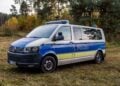Polizeibus mit Blaulichtbalken auf einer Wiese am Waldrand, dahinter Kiefern und herbstlich gefärbte Birken