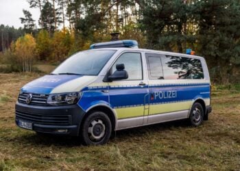 Polizeibus mit Blaulichtbalken auf einer Wiese am Waldrand, dahinter Kiefern und herbstlich gefärbte Birken