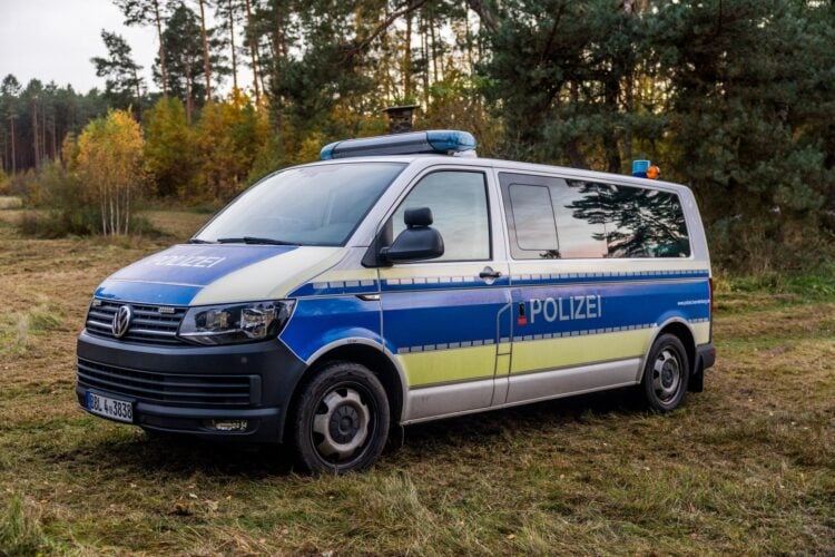 Polizeibus mit Blaulichtbalken auf einer Wiese am Waldrand, dahinter Kiefern und herbstlich gefärbte Birken