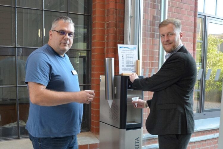 Zwei Männer mit Bechern an einem neuen Trinkwasserspender im Kreishaus in Forst (Lausitz)