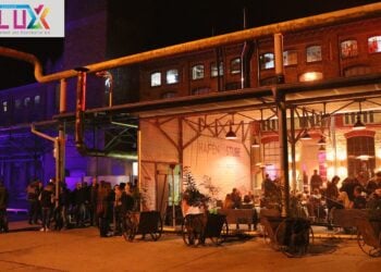 Die beleuchtete Hafenstube des SKZ Telux am Abend mit Gästen vor dem Industriegebäude
