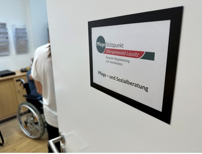 Tür des Pflegestützpunktes Oberspreewald-Lausitz mit Schild Pflege- und Sozialberatung, dahinter ein Beratungsraum mit Rollstuhl