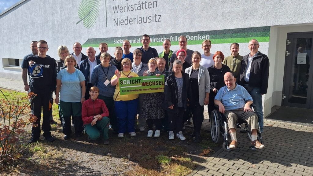 Gruppenfoto von Beschäftigten der Integrationswerkstätten Niederlausitz mit Bürgermeister Andreas Pfeiffer vor dem Werkstattgebäude