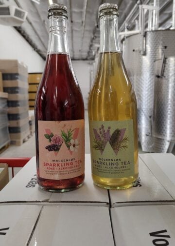 Je eine Flasche Wolkenløs Sparkling Tea Rosé und Weiß vor Edelstahltanks
