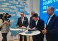 Vier Männer an einem Stehtisch auf einem Messestand, einer unterschreibt ein Dokument, dahinter eine Karte des Rheinischen Reviers