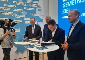 Vier Männer an einem Stehtisch auf einem Messestand, einer unterschreibt ein Dokument, dahinter eine Karte des Rheinischen Reviers