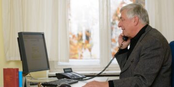 Ein ehrenamtlicher Mitarbeiter der Telefonseelsorge telefoniert an einem Schreibtisch mit Computer