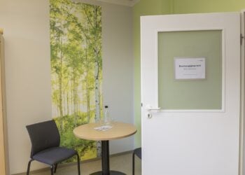 Beratungsraum mit Tisch, zwei Stühlen und Birkenwald-Tapete, an der geöffneten Tür ein Schild Beratungsgespräch