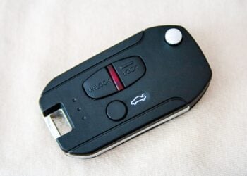 Schwarzer Klapp-Funkschlüssel eines Autos mit Tasten zum Ver- und Entriegeln auf hellem Stoff