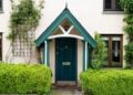 Eingang eines kleinen Hauses mit grüner Tür, Efeu an der Fassade und Pflanzen davor