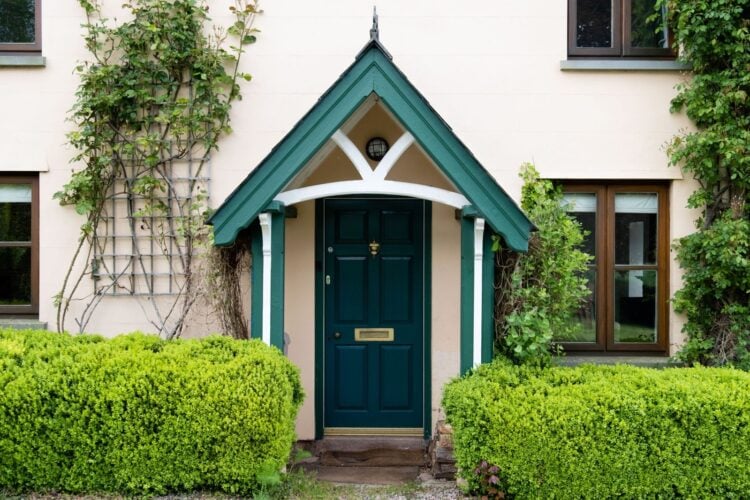 Eingang eines kleinen Hauses mit grüner Tür, Efeu an der Fassade und Pflanzen davor