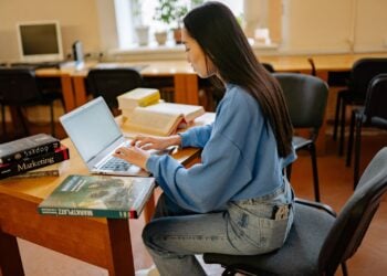 Frau arbeitet am Laptop, umgeben von Büchern und Notizen