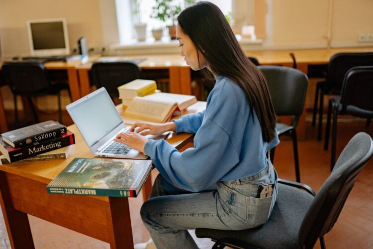 Frau arbeitet am Laptop, umgeben von Büchern und Notizen