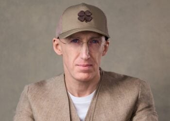 Porträt von Uri Poliavich mit beigefarbener Kappe, runder Brille und Leinensakko