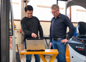 Zwei Mitarbeiter von Waury Fördertechnik an einem Laptop zwischen Gabelstaplern
