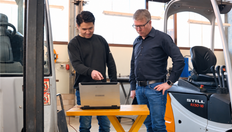 Zwei Mitarbeiter von Waury Fördertechnik an einem Laptop zwischen Gabelstaplern